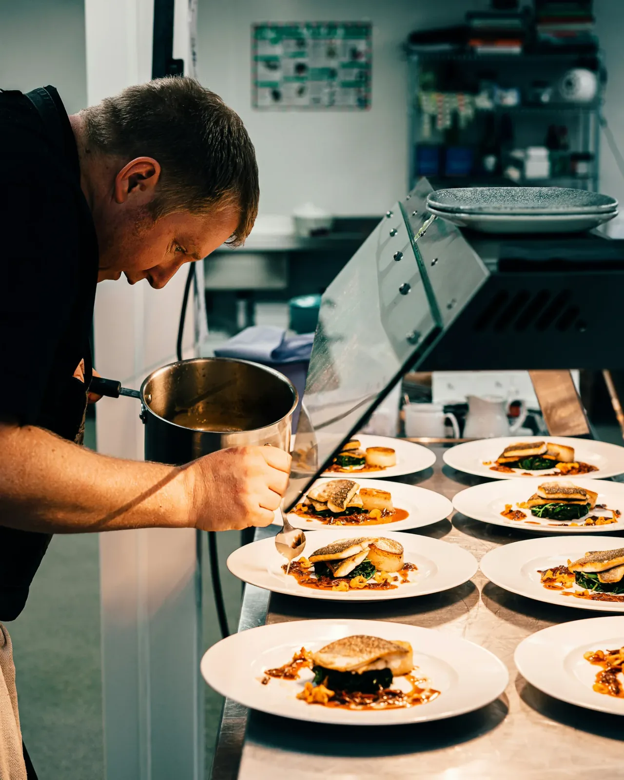 A chef finishing a row of dishes at the kitchen pass