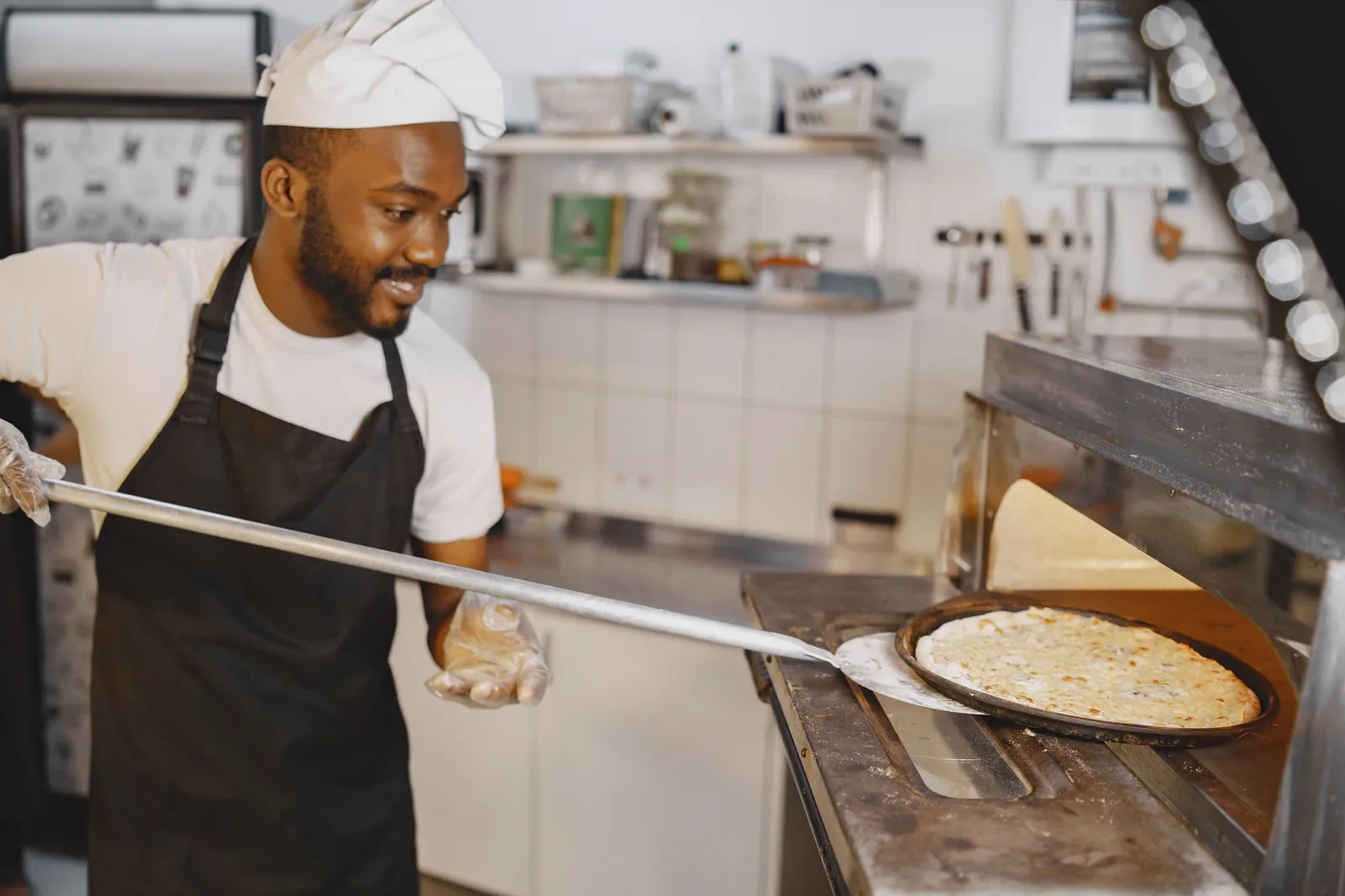 A cook lifting a pizza into the oven