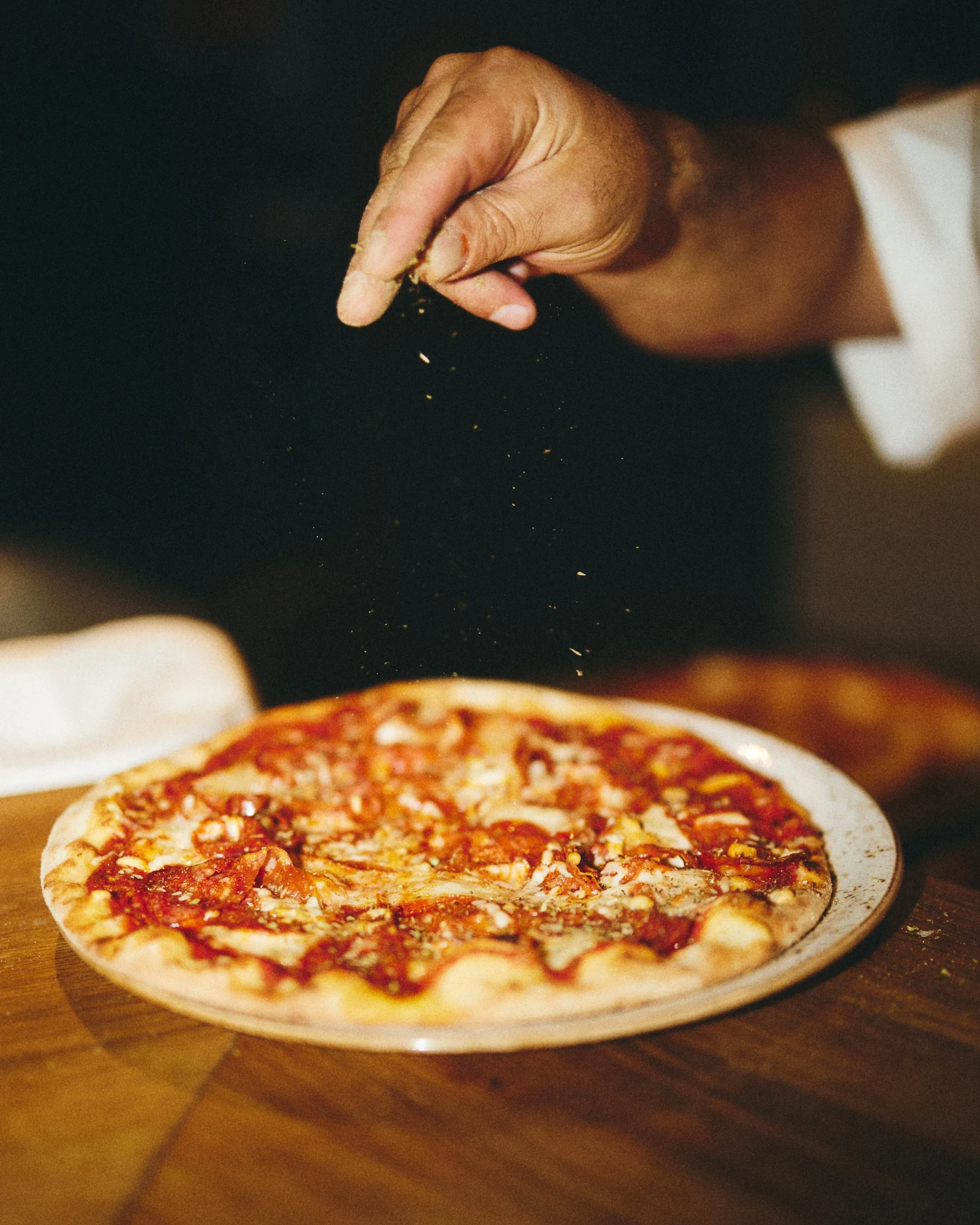 Krydderier drysses over en pizza hos Fresca Pizzeria i Paleet