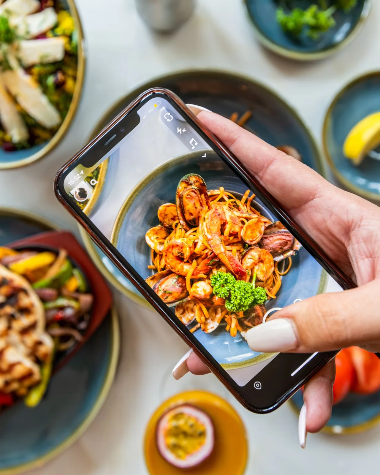 En gjest fotograferer en pastarett med mobilen ved et restaurantbord